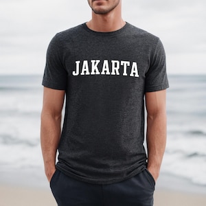 Puede incluir: Una camiseta gris oscuro jaspeada con la palabra "JAKARTA" impresa en blanco en la parte delantera.