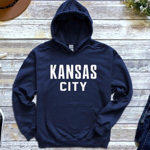 May include: A navy blue hooded sweatshirt with the text "KANSAS CITY" printed in white on the front.