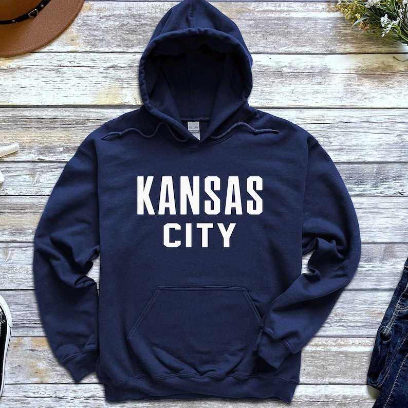 May include: A navy blue hooded sweatshirt with the text "KANSAS CITY" printed in white on the front.