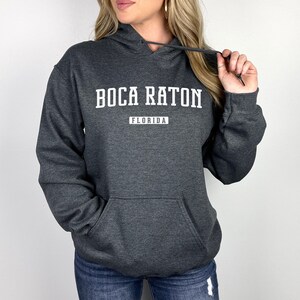 May include: A dark gray hooded sweatshirt with the text "Boca Raton, Florida" printed in white.