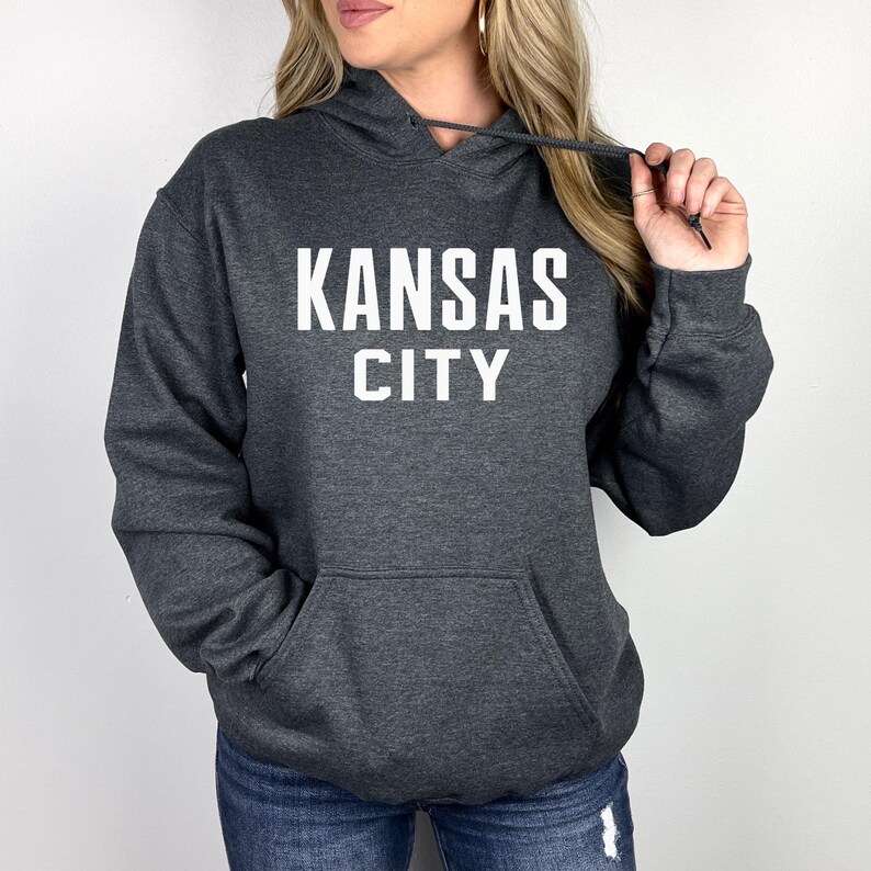 May include: A dark gray hooded sweatshirt with the text "KANSAS CITY" in white lettering.