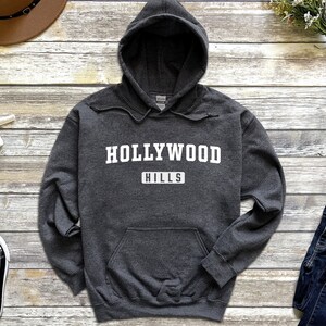 May include: A dark gray hooded sweatshirt with the text "HOLLYWOOD HILLS" in white lettering.