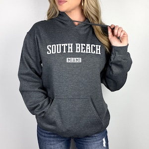 May include: A dark gray hooded sweatshirt with the text "SOUTH BEACH MIAMI" printed in white.