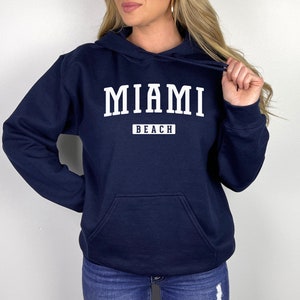 May include: A navy blue hoodie with a white print that says "MIAMI BEACH" in a collegiate font.
