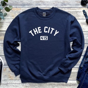 Op de afbeelding: Een marineblauw sweatshirt met witte tekst die "THE CITY 415" zegt.