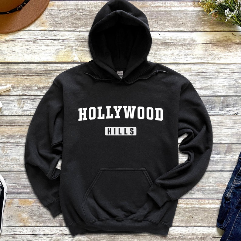 May include: Black hooded sweatshirt with white text that reads "HOLLYWOOD HILLS" in a collegiate font.