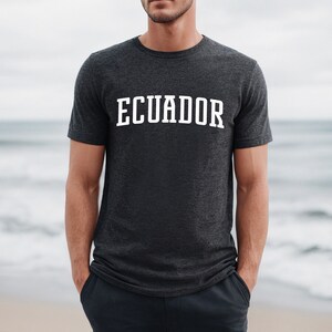 May include: A dark heather grey t-shirt with the word "ECUADOR" printed in white on the front.