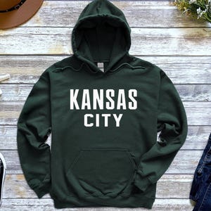 May include: A dark green hooded sweatshirt with the text "KANSAS CITY" in white lettering.