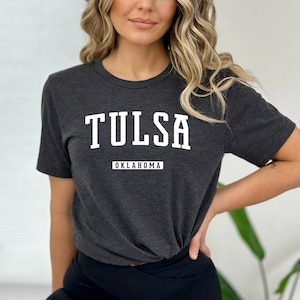 Könnte beinhalten: Ein dunkelgraues T-Shirt mit weißem Text, der "TULSA OKLAHOMA" lautet.