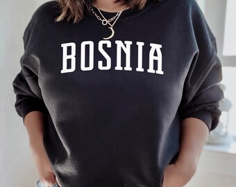 Könnte beinhalten: Schwarzer Pullover mit weißem Text, der "BOSNIA" in einer College-Schriftart lautet.