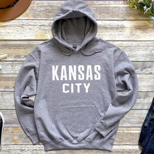 May include: A gray hooded sweatshirt with the text "KANSAS CITY" printed in white on the front.