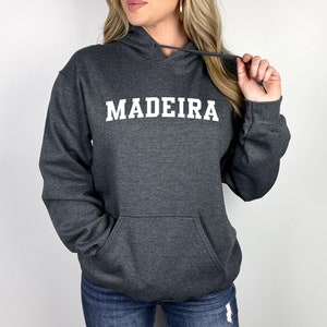 Puede incluir: Una sudadera con capucha gris oscuro con la palabra "MADEIRA" impresa en blanco en la parte delantera.