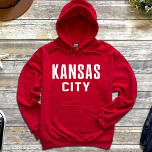 May include: Red hooded sweatshirt with the text "KANSAS CITY" in white lettering.