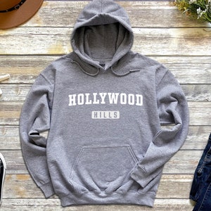 May include: A gray hooded sweatshirt with the text "HOLLYWOOD HILLS" printed in white on the front.