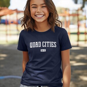 Puede incluir: Una camiseta azul marino con texto blanco que dice "QUAD CITIES IA-IL".