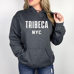 Könnte beinhalten: Ein dunkelgrauer Kapuzenpullover mit dem Aufdruck "TRIBECA NYC" in Weiß auf der Vorderseite.