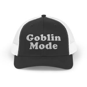 May include: Black and white trucker hat with a white mesh back. The front of the hat has the text "Goblin Mode" in white.