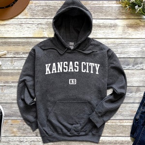 Puede incluir: Una sudadera con capucha gris oscuro con el texto "KANSAS CITY KS" en blanco.