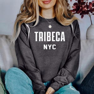 Könnte beinhalten: Ein dunkelgrauer Pullover mit dem Aufdruck "TRIBECA NYC" in Weiß auf der Vorderseite.