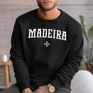 Puede incluir: Sudadera negra con texto blanco que dice "MADEIRA" y una cruz blanca debajo del texto.