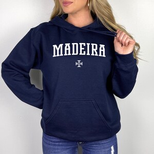 Puede incluir: Una sudadera con capucha azul marino con la palabra "MADEIRA" impresa en blanco y una cruz blanca.
