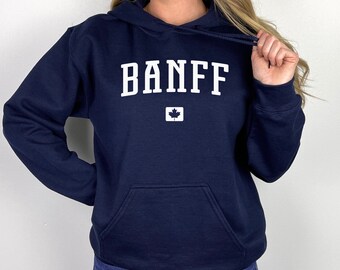 Puede incluir: Una sudadera con capucha azul marino con un gráfico blanco de "BANFF" y una pequeña bandera canadiense.