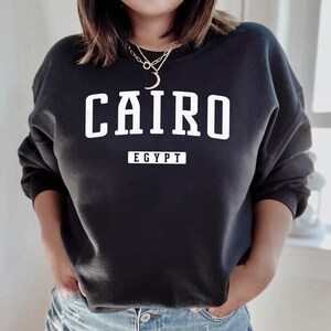 May include: Black sweatshirt with white text that reads "CAIRO EGYPT" in a vintage collegiate style font.