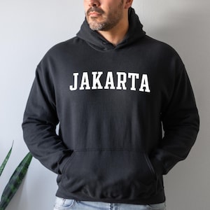 May include: Black hooded sweatshirt with the word "JAKARTA" printed in white on the front.