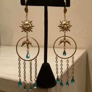 Puede incluir: Pendientes de oro con un dise&ntilde;o de sol y p&aacute;jaro, con cristales de l&aacute;grima turquesa colgando de cadenas.