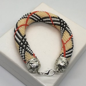 May include: A beige, black, white, and red beaded bracelet with silver end caps and a silver clasp.