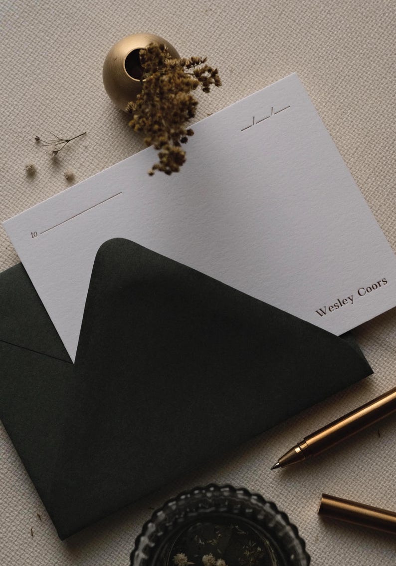 Puede incluir: Una tarjeta de papeler&iacute;a rectangular blanca con el nombre impreso Wesley Coors, que presenta una l&iacute;nea para texto que comienza con la palabra to. La tarjeta est&aacute; parcialmente insertada en un sobre negro, junto a un bol&iacute;grafo dorado.