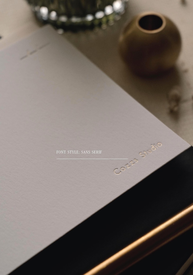 Puede incluir: Una tarjeta de papel rectangular de color gris claro con el texto dorado en relieve Cozzs Studio en una fuente sans serif. La tarjeta tiene una textura mate y lisa, y est&aacute; colocada en &aacute;ngulo, destacando las letras met&aacute;licas sobre la superficie.
