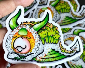 Può includere: Un adesivo disegnato a mano di un rotolo di sushi verde e giallo con un viso da cartone animato e una testa di drago verde. Il rotolo di sushi è decorato con semi di sesamo e un involucro di alga verde. L'adesivo è su uno sfondo bianco.