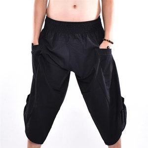 May include: Black, cropped harem pants with an elastic waistband and large side pockets. The pants are made of a lightweight fabric and are worn with black flip-flops.