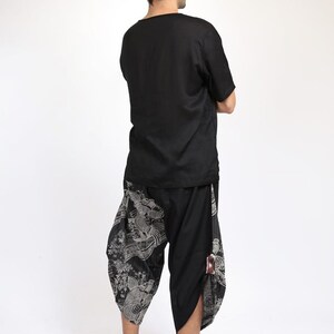 May include: A person wearing a black short-sleeved shirt and black pants with a white and gray print. The pants have a loose fit and are gathered at the ankles.
