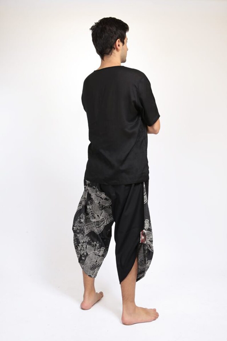 May include: A person wearing a black short-sleeved shirt and black pants with a white and gray print. The pants have a loose fit and are gathered at the ankles.