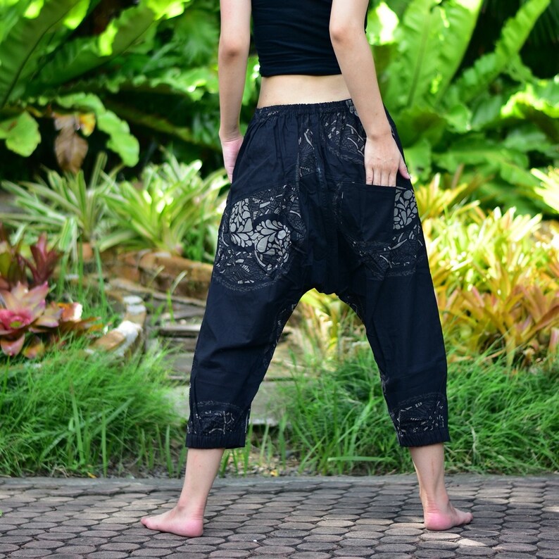 May include: Black cotton trousers with a floral pattern. The trousers have a loose fit and a wide leg.