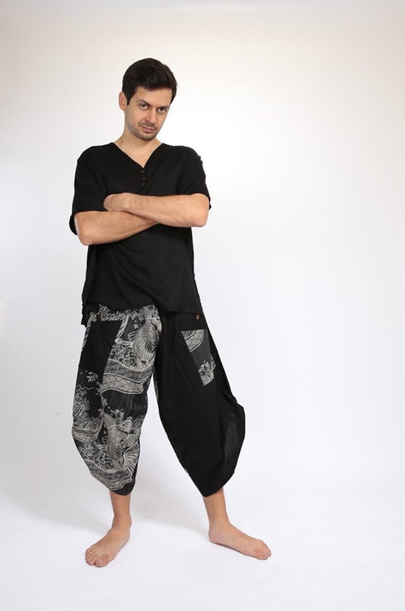 May include: A man wearing a black short-sleeved shirt with a v-neck and black pants with a white and gray patterned design.