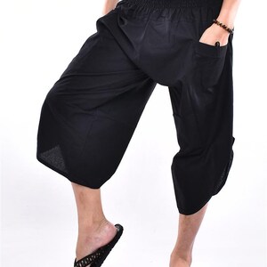 May include: Black, cropped, loose-fitting pants with an elastic waistband and pockets. The pants are paired with black flip-flops. The image is set against a white background.