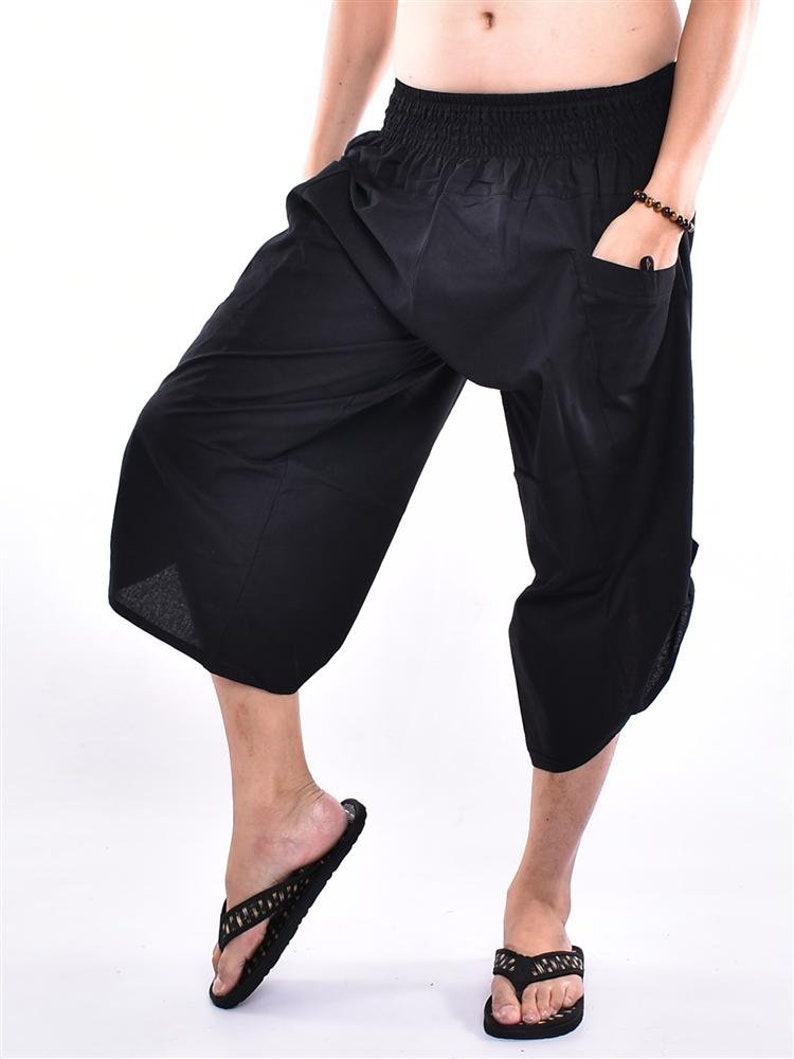 May include: Black, cropped, loose-fitting pants with an elastic waistband and pockets. The pants are paired with black flip-flops. The image is set against a white background.
