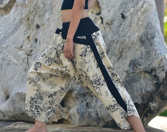 May include: A pair of cream-colored pants with a black trim and a floral pattern. The pants are loose-fitting and have a wide leg.