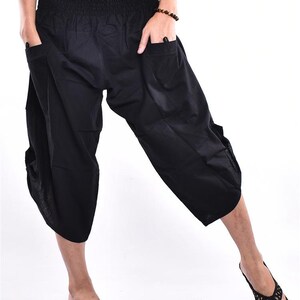 May include: Black, cropped harem pants with an elastic waistband and pockets. The pants are made of a lightweight fabric and have a relaxed fit. The model is wearing black flip-flops. The pants are suitable for casual wear.