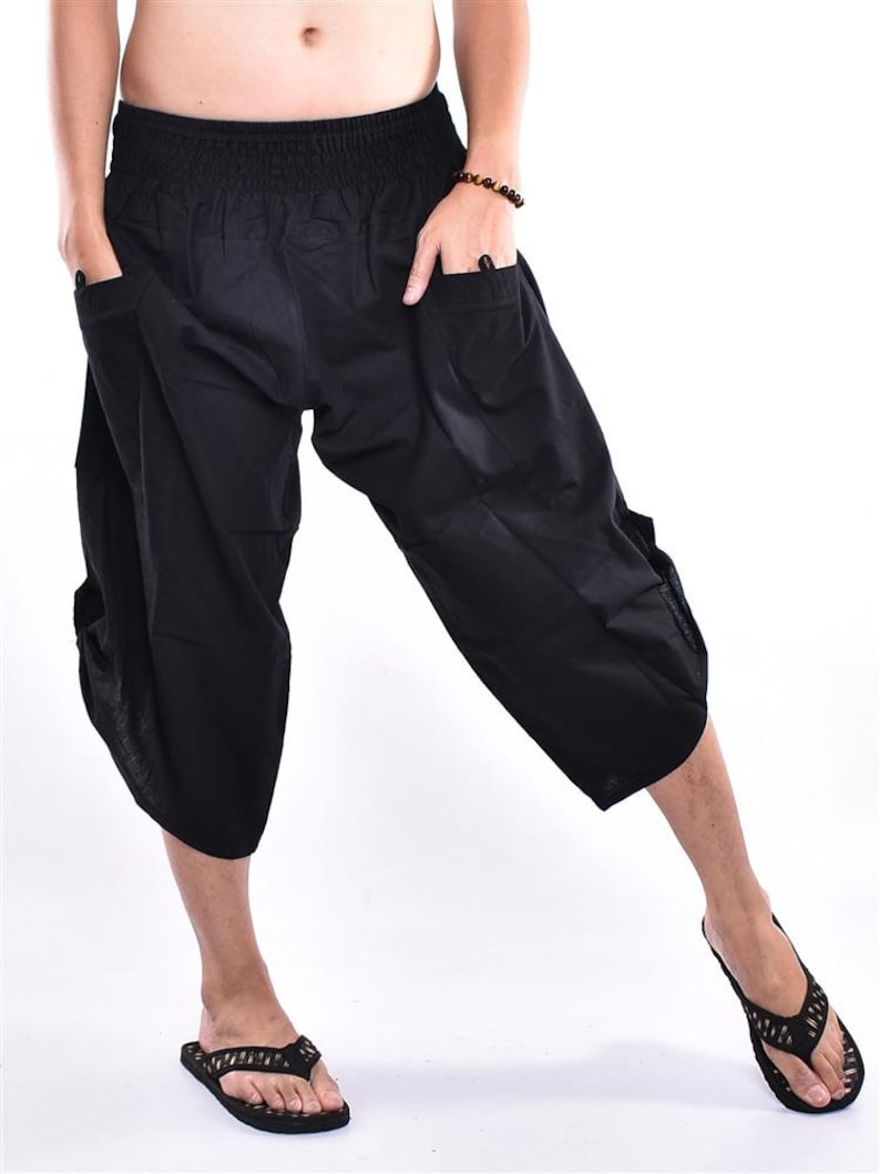 May include: Black, cropped harem pants with an elastic waistband and pockets. The pants are made of a lightweight fabric and have a relaxed fit. The model is wearing black flip-flops. The pants are suitable for casual wear.