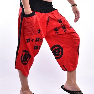 May include: Red pants with a black elastic waistband and black and white Japanese characters printed on them. The pants have a large pocket on the left side.