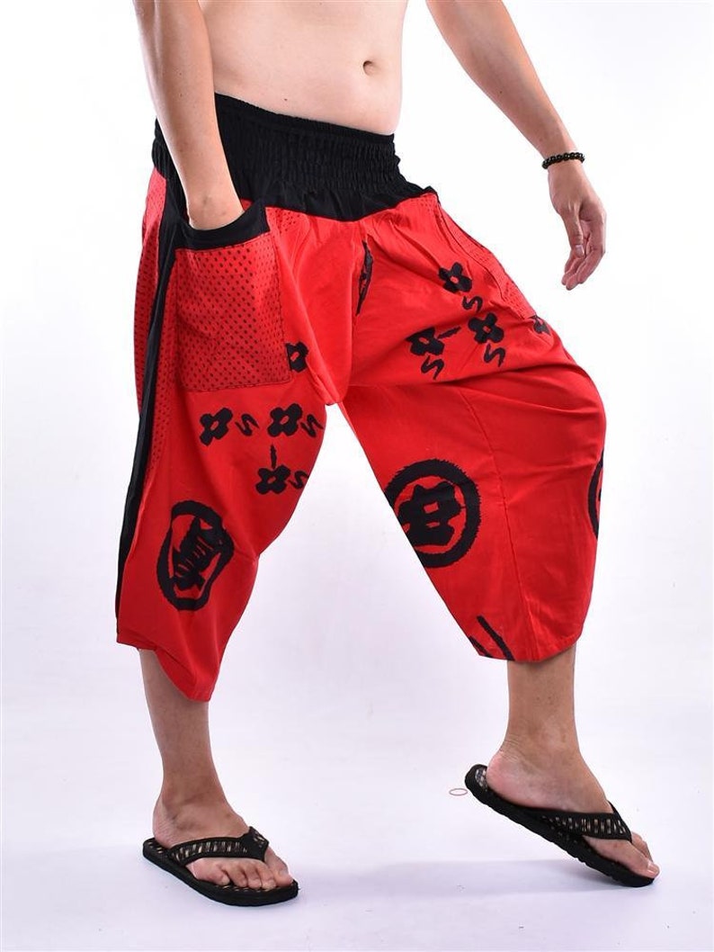 May include: Red pants with a black elastic waistband and black and white Japanese characters printed on them. The pants have a large pocket on the left side.