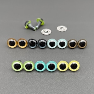 May include: A collection of colorful plastic craft eyes in various shades, including gold, brown, teal, and green, with black pupils. The eyes are arranged in rows, with metal washers and fasteners visible. Ideal for crafting and toy making.