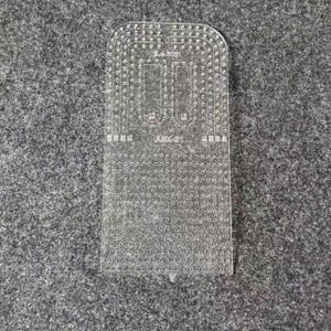 Peut inclure: Un gabarit de maroquinerie en acrylique transparent dot&eacute; d'une grille de petits trous pour la couture, avec des coins sup&eacute;rieurs arrondis. L'outil porte l'inscription 5.4 mm et ABX-01, ainsi que divers indicateurs num&eacute;riques pour l'espacement.