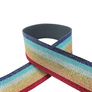 May include: A wide, flat elastic band featuring a repeating horizontal striped pattern in metallic shades of dark blue, light blue, silver, gold, and red. The reverse side of the fabric band is a solid, matte dark gray color with a textured weave.
