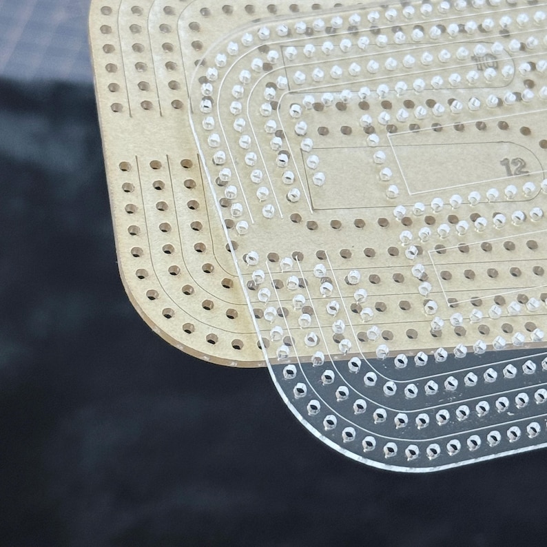 Peut inclure: Un gabarit en acrylique transparent pour le travail du cuir, dot&eacute; de coins arrondis et d'une s&eacute;rie de trous r&eacute;guli&egrave;rement espac&eacute;s sur les bords. Le gabarit est superpos&eacute; sur un mat&eacute;riau de base beige avec les chiffres 10 et 12 imprim&eacute;s.