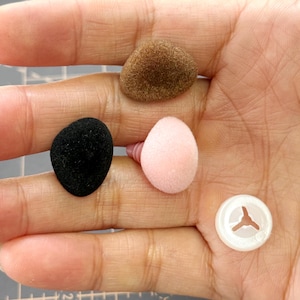 Può includere: Un assortimento di materiali per il fai-da-te: tre forme arrotondate in peluche marrone, nero e rosa, più un fermaglio di plastica bianco. Questi elementi sono probabilmente utilizzati per la creazione di bambole o altri progetti creativi.